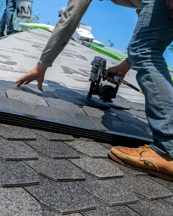 A roofer nailing an asphalt shingle into place